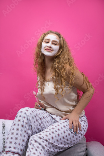 A girl with a cosmetic mask on her face sits on the sofa.
