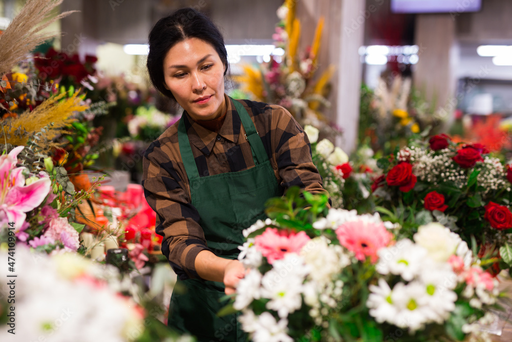 Asian female florist carefully examines bouquets in a flower shop, checking them for freshness