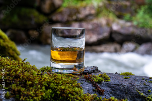 Fototapeta Glass of strong scotch single malt whisky with fast flowing mountain river on ba