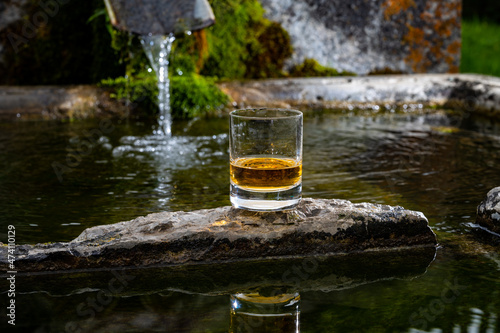 Glass of strong scotch single malt whisky served on old stone reservoir for water from mountain spring