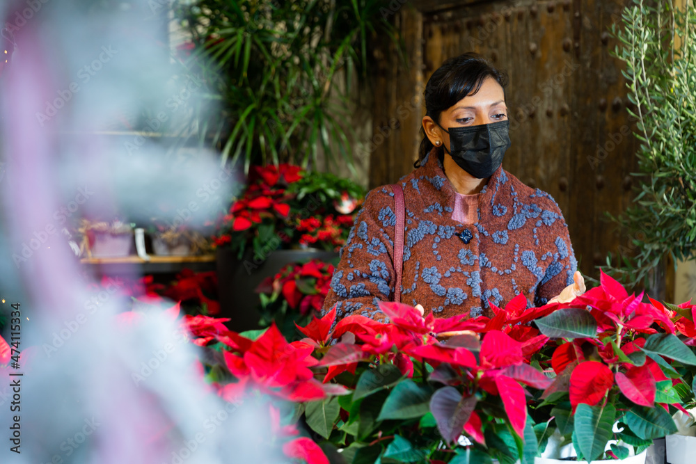 Adult Latin woman in face mask choosing plants in house plants shop.