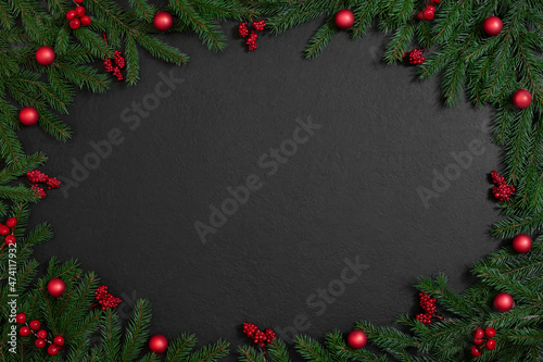 Christmas frame with fir branches and red berries  baubles on a black background. Xmas greeting card. Happy New Year. Copy space  top view  flat lay.
