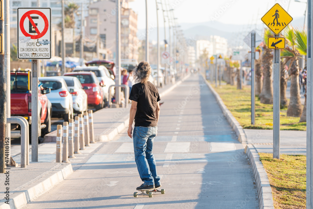 latin mature or senior man skateboard on bikeway in La Serena at sunset	