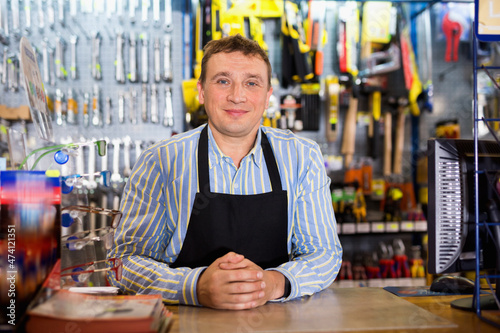 Positive cheerful smiling seller standing in hardware shop photo