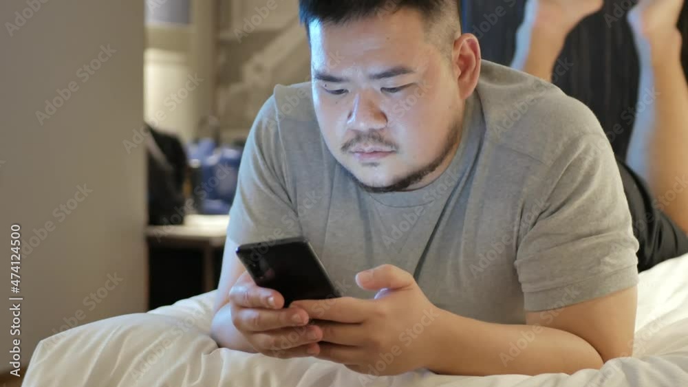 asian man while using chatting on mobile phone and lay on the bed in bed room asian man while using chatting on mobile phone and lay on the bed in bed room
