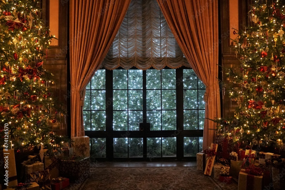 A beautiful room with large glass window, tall curtains and Christmas trees