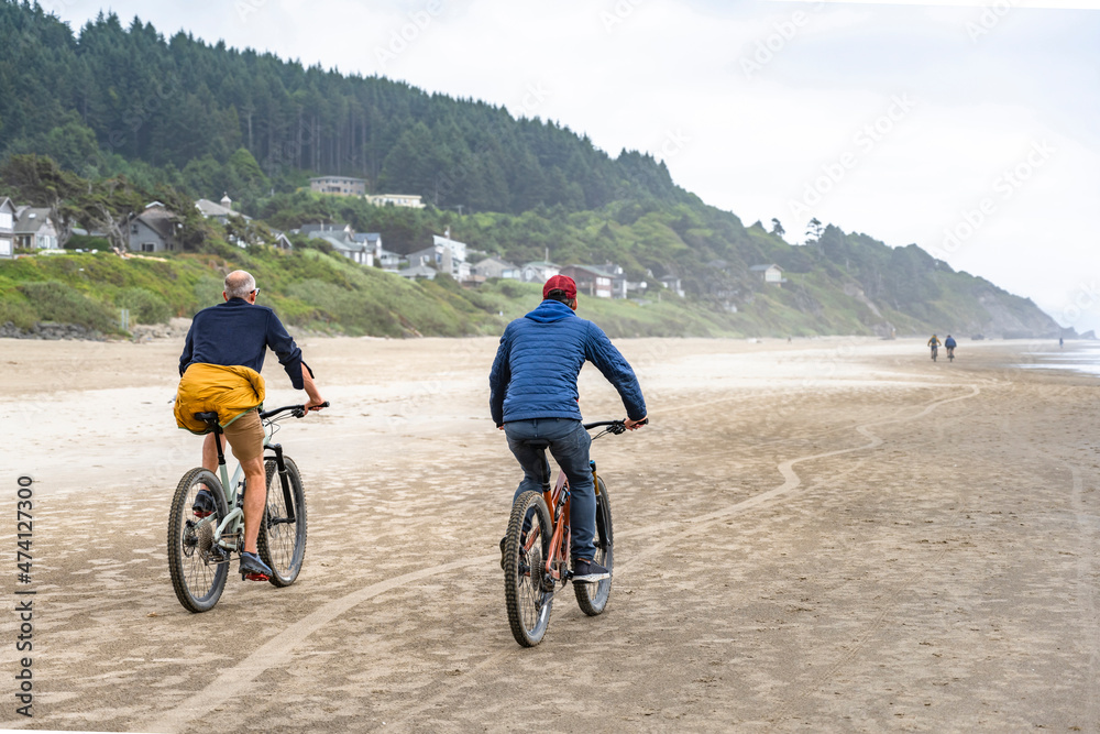 An elderly father and a young son travel side by side on bicycles along the Pacific Ocean preferring an active healthy lifestyle tempering the body in any weather