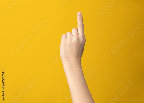 Female hand gesture shows one index finger on yellow background isolated