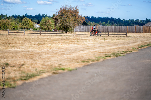 Man rides an electric hybrid bike on a path with a wooden fence preferring an active healthy lifestyle