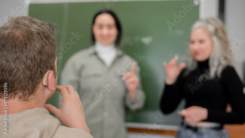 Two girls and a guy are talking in sign language. Three deaf students chatting in a university classroom.