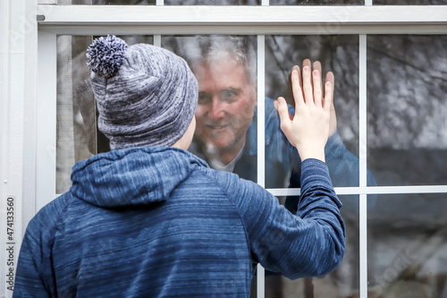 Teen visiting senior citizen safe in home, touching hands through the window