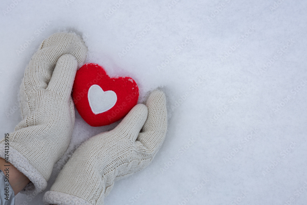 Women's hands in knitted mittens with a red heart on the snow on a winter day. Love concept. Valentine day background