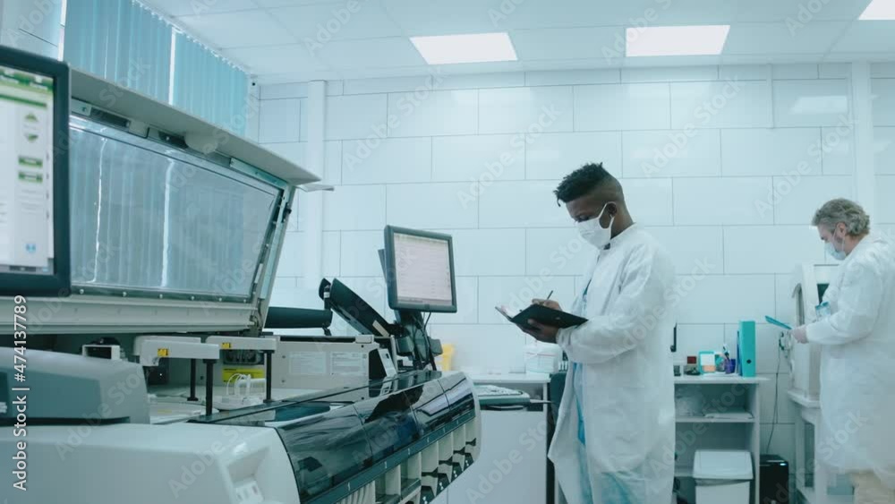 A diverse team works in the lab using tablet computers, wearing masks and gowns. Black male laboratory assistant watching how robot works. Work in the laboratory. High quality 4k footage A diverse team works in the lab using tablet computers, wearing masks and gowns. Black male laboratory assistant watching how robot works. Work in the laboratory. High quality 4k footage