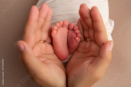 The palms of the father, the mother are holding the foot of the newborn baby in a white blanket. Feet of the newborn on the palms of the parents. Studio photography of a child's toes, heels and feet.