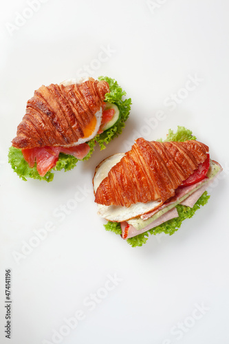 Two croissant sandwiches with fried eggs, salted salmon, ham, fresh cucumbers, tomatoes and lettuce