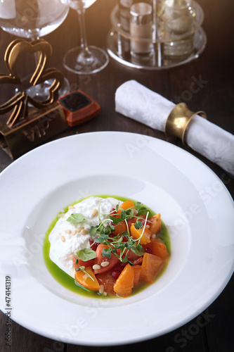 Straciatella with persimmon and tomatoes. Food on a white plate. Restaurant menu concept.Festive table setting.Vertical photo.Top view with copy space. Flat lay.