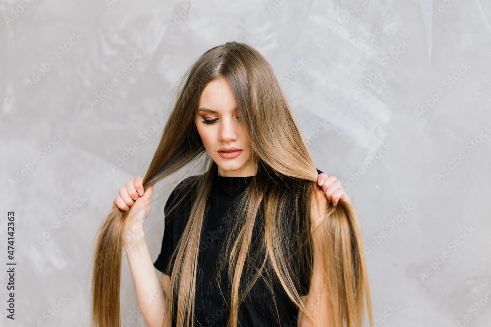 Girl touching her hair and smiling while posing at interior looking in the mirror Girl touching her hair and smiling while posing at interior looking in the mirror