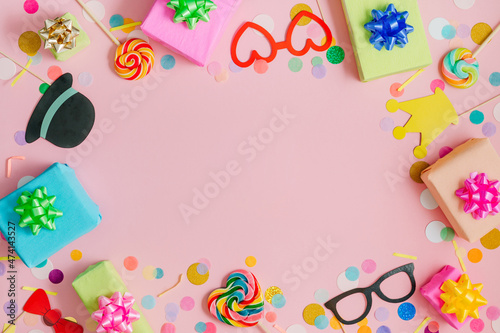 Heart shaped lollypop and decorative paper eye glasses, gift boxes on pink background with confetti