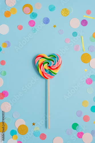 Multicolored heart shape lollypop on the blue background with confetti