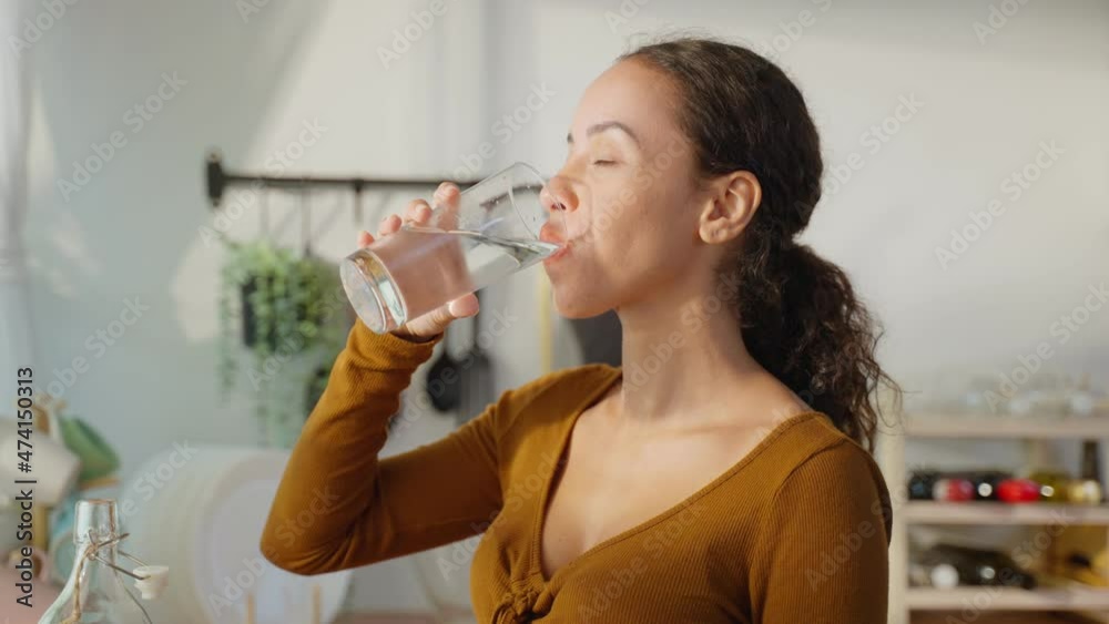 Young beautiful Latino woman holding clean water into glass in kitchen. Young beautiful Latino woman holding clean water into glass in kitchen.