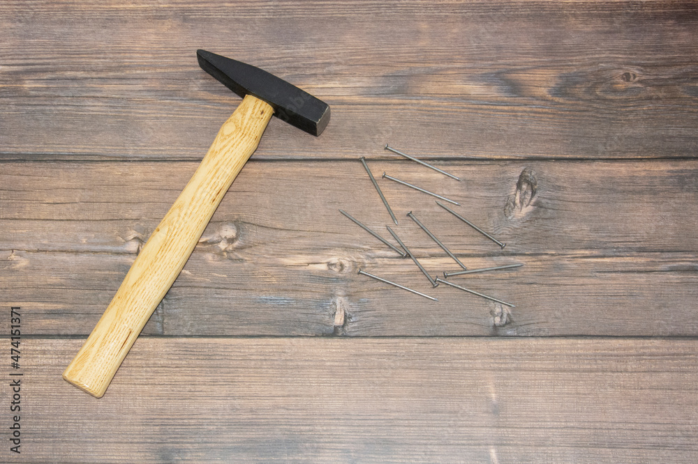 A construction hammer with a wooden handle lies on the brown floor to the left. Hammer and nails on wooden, brown boards.
