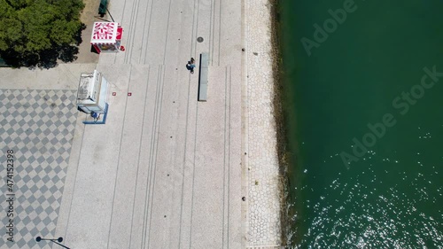 Aerial view following a woman riding a bike, in sunny Lisbon, Portugal - high angle, drone shot