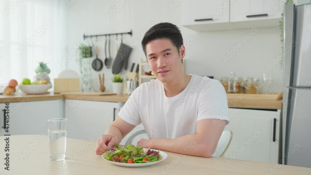 Portrait of Asian male look at camera while eat green salad in kitchen. Portrait of Asian male look at camera while eat green salad in kitchen.