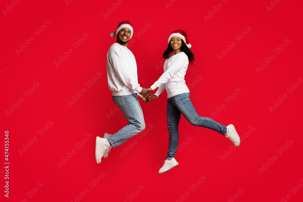 Beautiful black couple in Santa hats holding hands and jumping