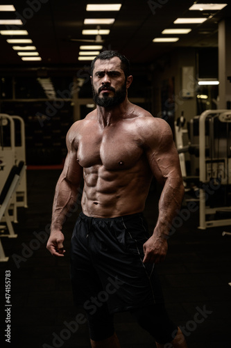 strong young male with beard and perfect fitness abdominal muscles in sport gym in night
