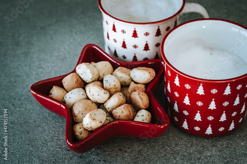 Christmas eve background. Traditional cookies kuciukai in red star shaped vase and two cups of coffee cappuccino or latte. Mugs decorated with Xmas ornaments. Winter holidays concept. photo