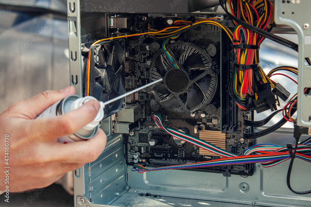 Maintenance and cleaning of the insides of the computer. Man's hand holds a cylinder of compressed air and cleans the insides of the computer