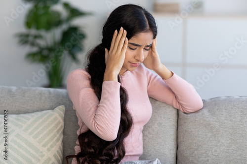 Tableau sur toile Despaired upset young hindu female suffer from headache and flu, sits on sofa an