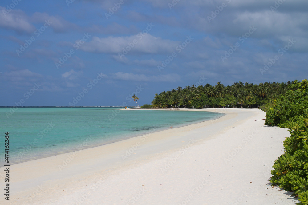 Morning on the shores of the Indian Ocean with white sand, azure water, vacationers, bushes and palm trees against a blue sky with clouds