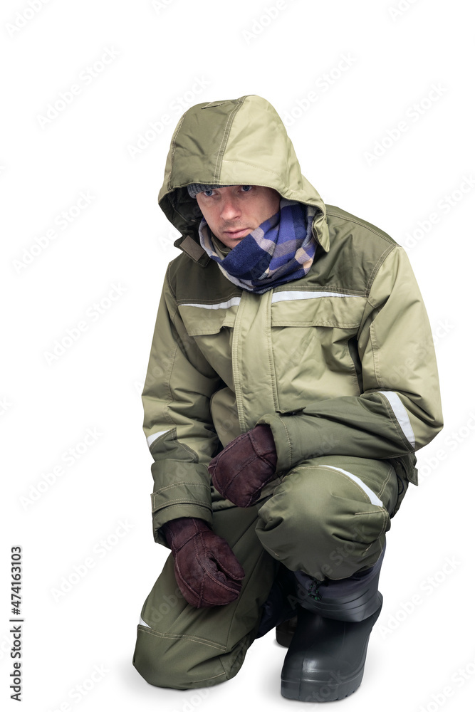 Man in warm winter clothing for frosty and cold weather. Fisherman or worker for cleaning snow on a white isolated background. Squatting Man in warm winter clothing for frosty and cold weather. Fisherman or worker for cleaning snow on a white isolated background. Squatting