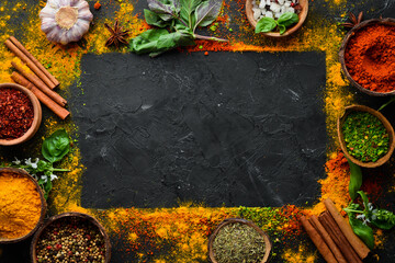 Colorful herbs and spices for cooking. Indian spices. On a black stone background. Top view.