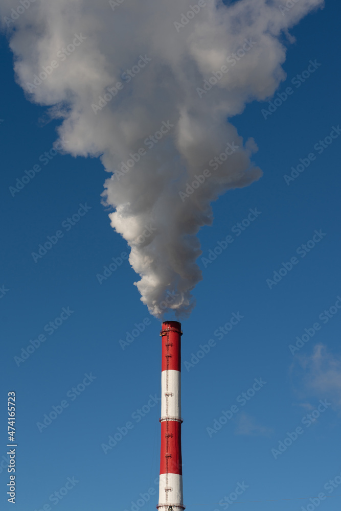 Vertical photo of smoking pipes of thermal power plant against sky. Fuming chimneys of a factory polluting