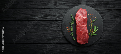 Raw sirloin steak with thyme, rosemary and spices. Top view. Flat lay top view on black stone cutting table. photo