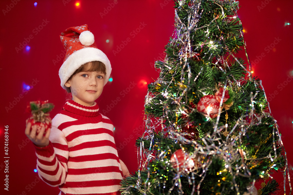 Christmas eve happy little girl in red striped pajamas decorates the christmas tree Christmas eve happy little girl in red striped pajamas decorates the christmas tree