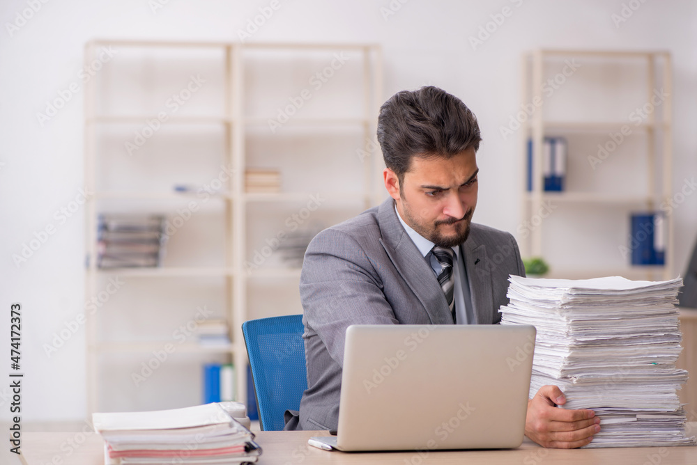 Young male employee unhappy with excessive work in the office Young male employee unhappy with excessive work in the office