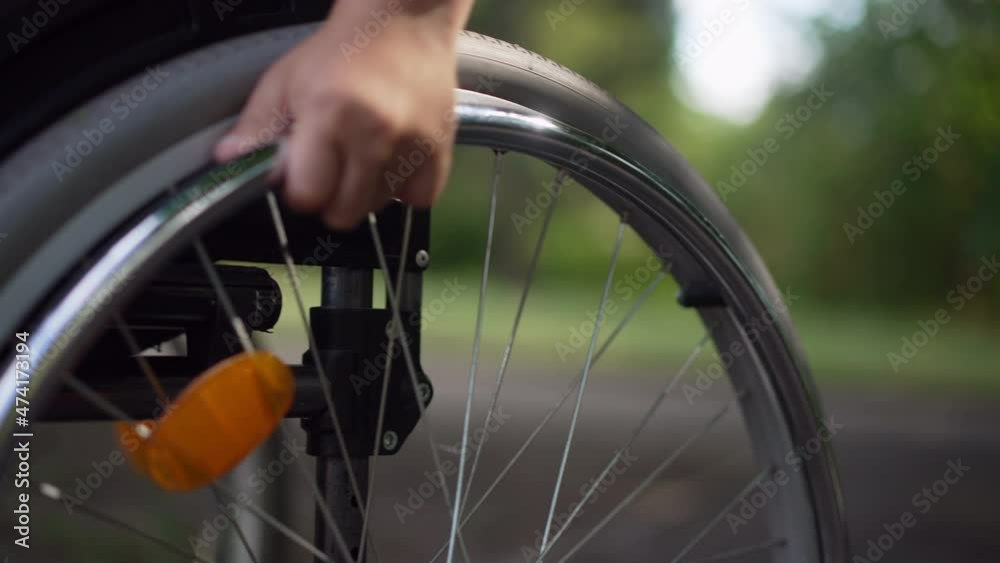 Close-up child hand rolling wheel of wheelchair in slow motion leaving. Unrecognizable Caucasian little disabled boy riding manual assistive device outdoors in summer park Close-up child hand rolling wheel of wheelchair in slow motion leaving. Unrecognizable Caucasian little disabled boy riding manual assistive device outdoors in summer park