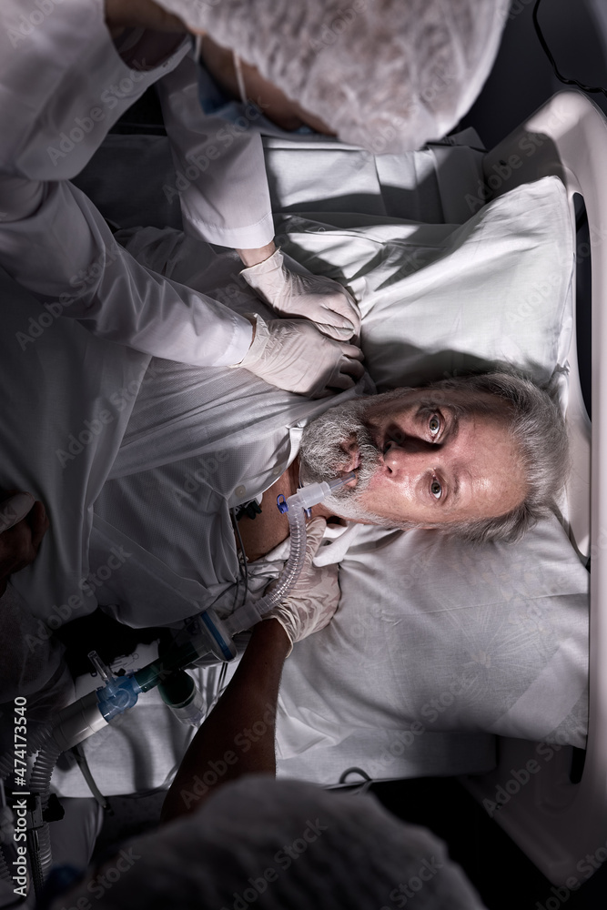 senior sick man woke up at night with high blood pressure, after surgery, with medical equipment in mouth, lying in hospital ward after operation, at night time. doctors help. top view