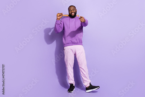 Full length body size view of attractive cheerful cool guy holding bat pointing at you isolated on violet purple color background