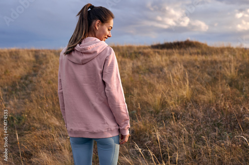 Rear view on happy female in pink hoodie and leggins standing in field in the morning. view from back on long-haired lady going to train on fresh air outdoors, at sunrise. people lifestyle concept © alfa27