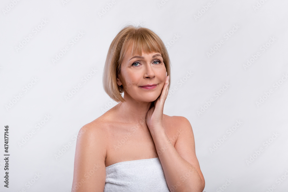 Beautiful senior woman in towel after bath touching her silky soft skin on light studio background Beautiful senior woman in towel after bath touching her silky soft skin on light studio background