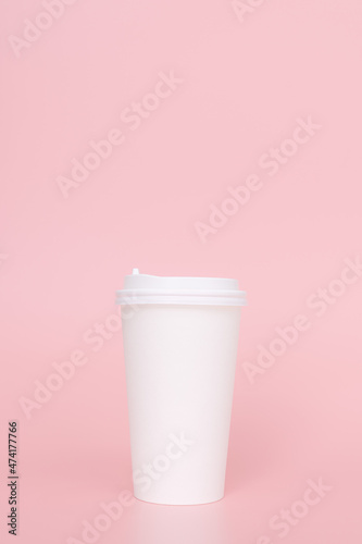 Take-out coffee with a white lid on top of a pink background.