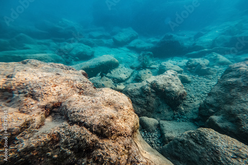 A deserted but fascinating underwater landscape with large rocks  reflections from the setting sun and small shoals of fish in shallow water. Narrow depth and soft focus