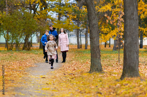 Children run along path in autumn park. They play and laugh, they have a lot of fun. Beautiful nature and trees with yellow leaves.