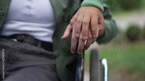 Unrecognizable boy holding hand of disabled girl on wheelchair armrest. Close-up palms of caring empathetic child and paralyzed friend outdoors in summer park. Support and friendship photo