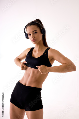 Confident active healthy woman in sports clothing posing isolated on white, looking down, listen to musicm copy space for advertisement. Attractive caucasian lady in black sportswear engaged in sport