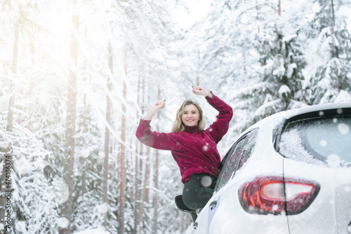 woman in a red sweater leaned out of the car window on a winter road in the woods, smiles